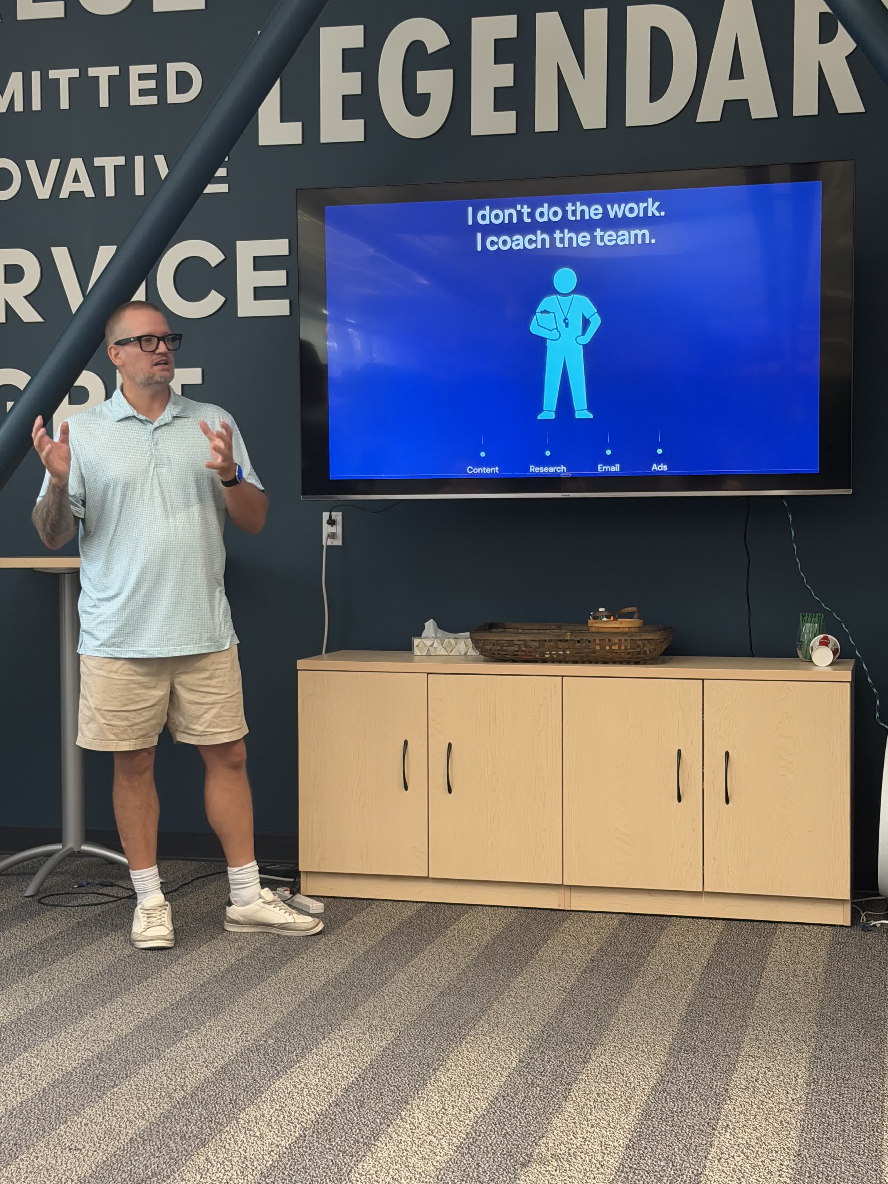 Wesley Cable speaking beside a presentation screen at his Granite Bay BNI chapter meeting, hands raised mid-gesture, with a slide reading 'I don't do the work. I coach the team.'